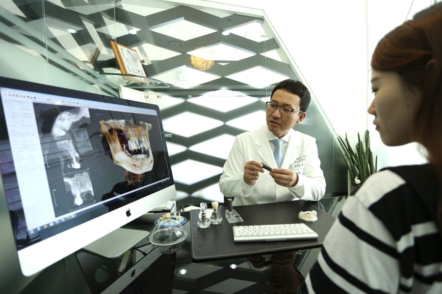 강남임플란트 — 치과 상담실에서 파노라마·CT 영상을 보며 치료 과정을 설명받는 장면