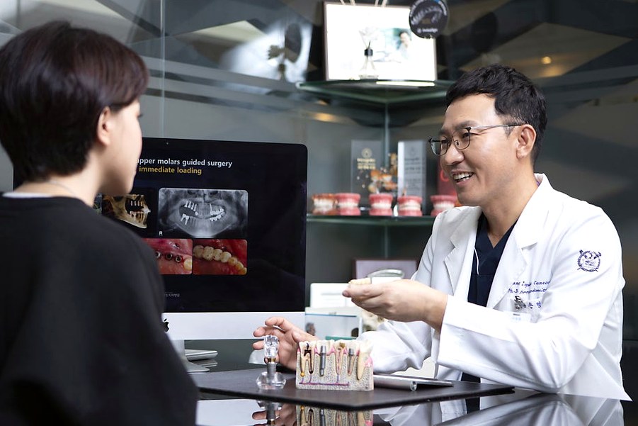 강남 오스템 임플란트 — 치과 상담 데스크에서 임플란트 모형을 두고 설명하는 장면